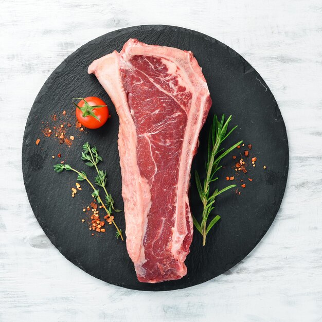 Raw New York steak with spices and herbs on a white wooden background. Flat lay. Top view.