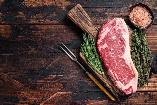 Foto bistecca di manzo cruda della striscia di new york o controfiletto su una tavola di legno. fondo in legno scuro. vista dall'alto. copia spazio.