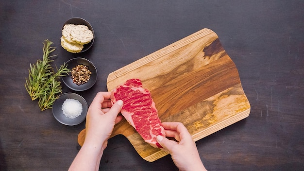 Raw New York strip steaks on a wood cutting board.