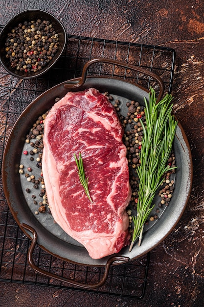 Raw New York or striploin beef meat steak with rosemary and pepper Dark background Top view