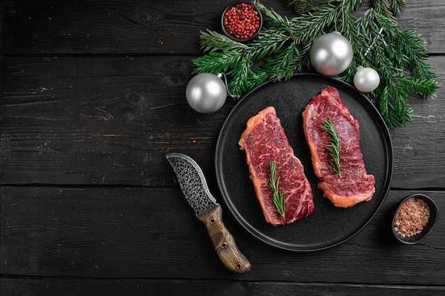 원시 뉴욕 스트립로인 쇠고기 스테이크는 크리스마스와 새해 세트로, 검은색 나무 테이블 배경, 위쪽 전망 플랫 레이, 텍스트 복사 공간