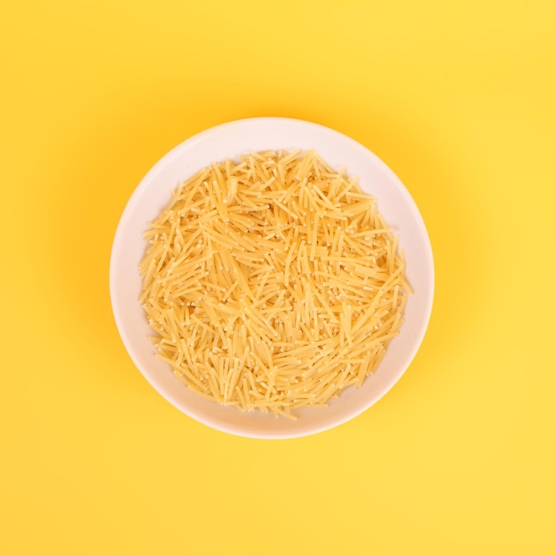 Raw noodles in a bowl on the yellow background