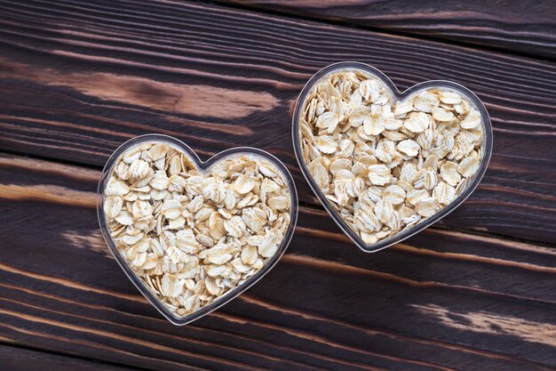 Raw oat-flakes on dark wood table. Uncooked cereal in bowls at heart shaped.