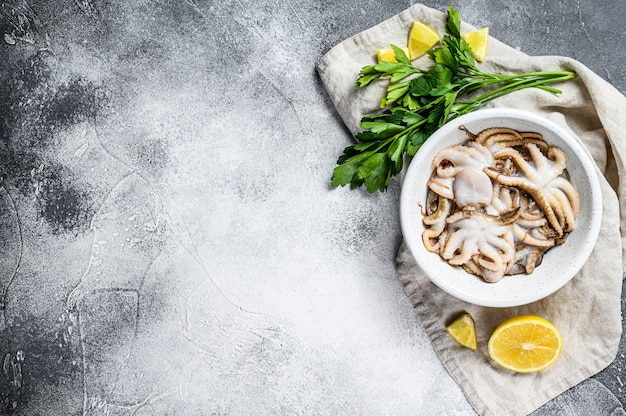 Raw octopus with parsley and lemon in a white bowl. Organic seafood. Gray background. Top view. Space for text