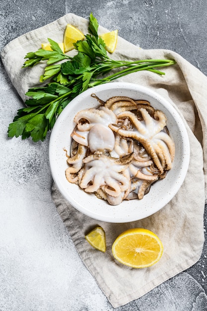 Raw octopus with parsley and lemon in a white bowl. Organic seafood. . Space for text