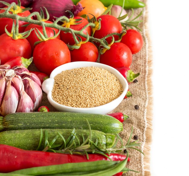 Raw organic amaranth in bowl with raw vegetables close up isolated on white with copy space