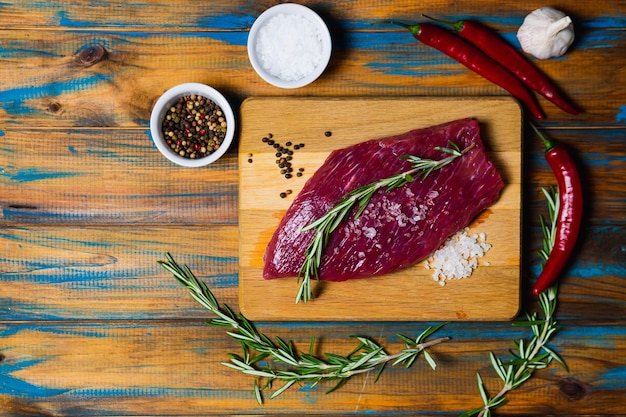 Raw organic beef meat with rosemary seasonings salt and red pepper on wooden background