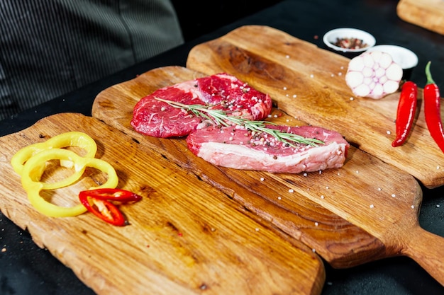 Raw organic beef meat with rosemary seasonings salt and red pepper on wooden cutting board