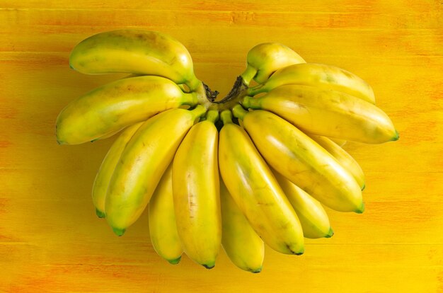 Raw organic bunch of baby bananas on old yellow wooden background