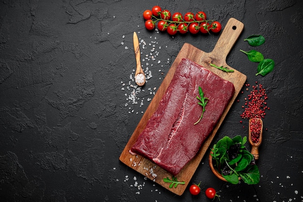 Photo raw organic marbled beef with spices on a wooden cutting board on a black slate stone or concrete background top view with copy space