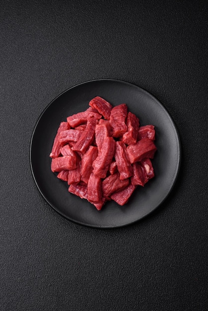 Raw organic meat beef or lamb cut into slices with salt spices and herbs on a dark concrete background