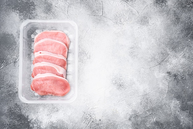 Foto carne biologica cruda. bistecche di maiale, filetti per grigliare, cuocere al forno o friggere, in contenitore di plastica, su sfondo grigio tavolo in pietra, vista dall'alto piatta, con copia spazio per il testo