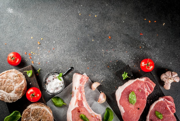 Raw organic meat. Selection of several types of red meat: pork cutlet on bone, pork steaks and chicken cutlets in grid of pork fat. With ingredients for cooking, gray stone table   top view