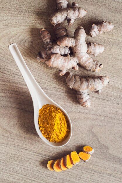 Raw organic orange turmeric root and powder in the spoon on wooden background Indian oriental low cholesterol spices Diet nutrition health care concept Vertical orientation flatlay