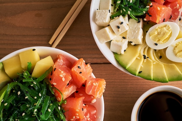 Poke organico crudo lancia con con riso, avocado, salmone, sulla vista superiore del fondo di legno