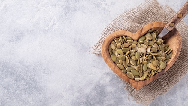 Raw organic pumpkin seeds in a wooden bowl. Top view. Copu space