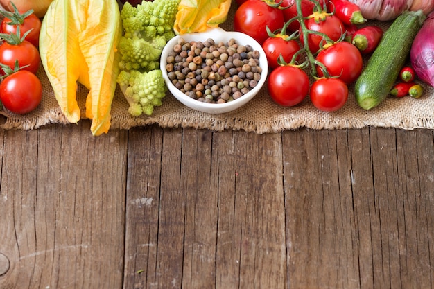 Raw organic roveja beans in a bowl with raw vegetables on a wooden table close up with copy space