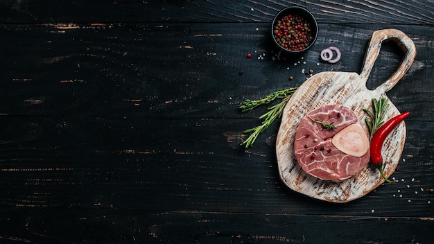 Carne cruda del marmo della bistecca di ossobuko con le erbe e le spezie su fondo scuro banner, menu, posto ricetta per testo, vista dall'alto