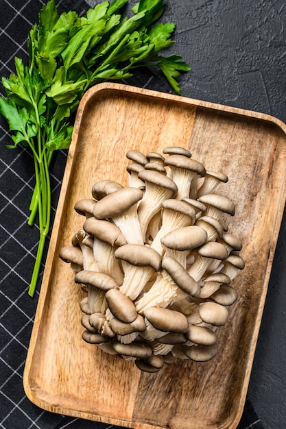 Raw oyster mushrooms in a wooden bowl with parsley. Organic food. Top view