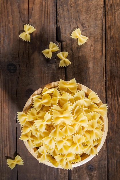 Photo raw pasta farfalle in wooden bowl on dark rustic background