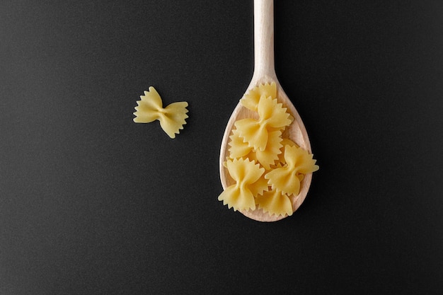 Raw pasta farfalle on wooden spoon on black background