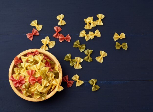 Raw pasta in the form of bows in a wooden round plate and white textile napkin