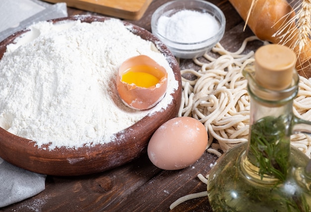 木製のテーブルに生パスタと食材。側面図。麺、小麦粉、オリーブオイル。