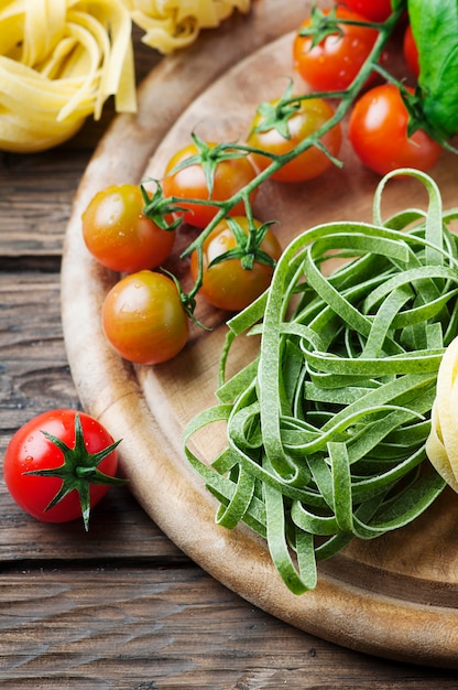 Raw pasta, tomato and basil on the wooden table