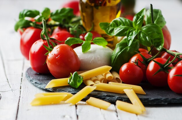 Raw pasta, tomatoes, mozzarella and basil leaves
