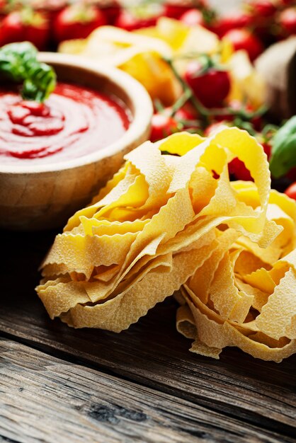 Raw pasta with ingredients on wooden table