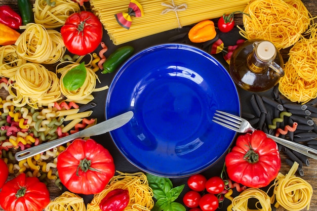 Pasta cruda con ingridients e copia spazio sul piatto blu vuoto con forchetta e coltello in acciaio