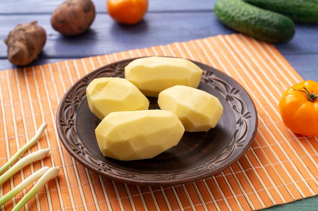 Raw peeled potato tubers on a plate on the kitchen table with vegetables. Preparation for cooking.