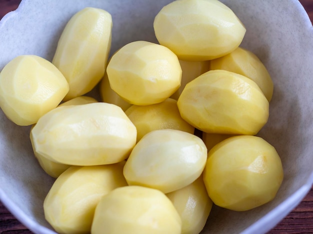 Raw peeled potatoes in a bowl on a dark wooden background.