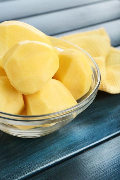 Raw peeled potatoes in glass bowl on color wooden background