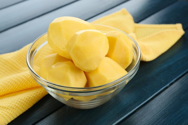 Raw peeled potatoes in glass bowl on color wooden background