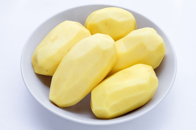 Raw peeled potatoes in white bowl on white background