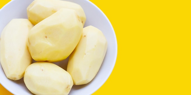 Raw peeled potatoes on yellow background