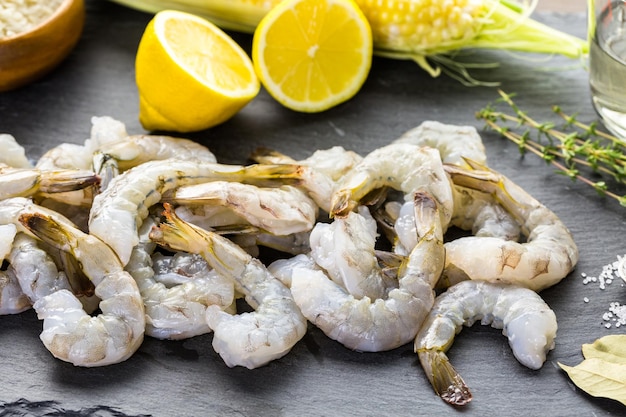 Raw peeled shrimp with tails with lemon on sutting board.