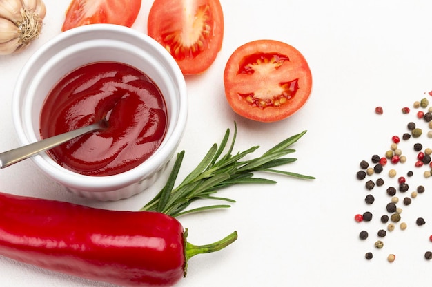 Raw pepper, allspice and rosemary on table. Tomato sauce in bowl. Copy space. White background. Top view