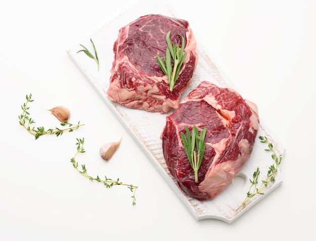 Raw piece of beef ribeye with rosemary thyme on a white table top view