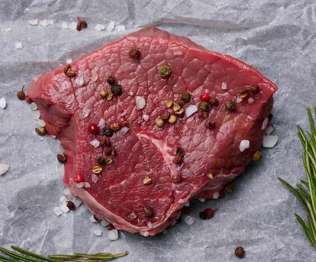 Raw piece of beef with spices lies on a white piece of parchment paper top view