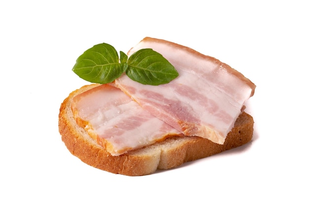 A raw piece of fresh bacon with a green basil leaf on a piece of white wheat bread