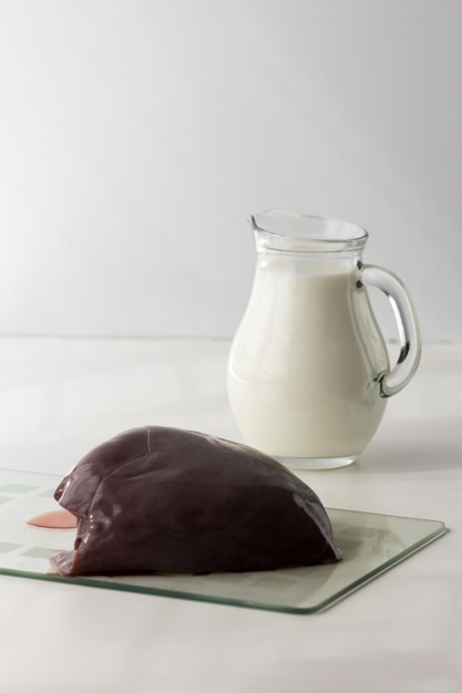 Raw pieces of liver on glass cutboard jar with milk on the white background