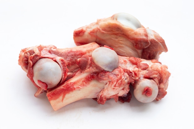 Raw pig bone in white bowl on white background.