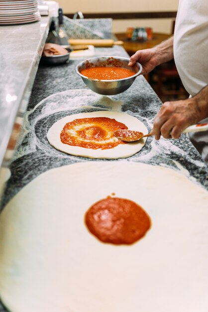 Raw pizza dough with tomato sauce. Chef adding sauce.