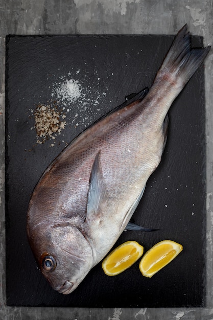 Photo raw porgy fish with lemon on black ceramic