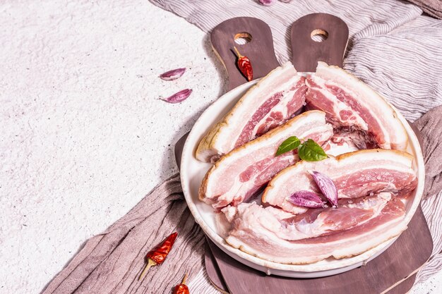 皮、腹膜肉を添えた生の豚バラ肉。スパイスやハーブ、健康的な食事を調理するための材料、動物性タンパク質。明るい漆喰の背景、コピースペース