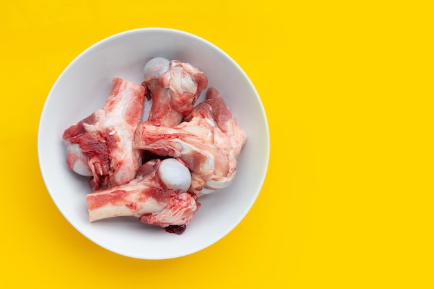 Raw pork bones in white bowl on yellow background.