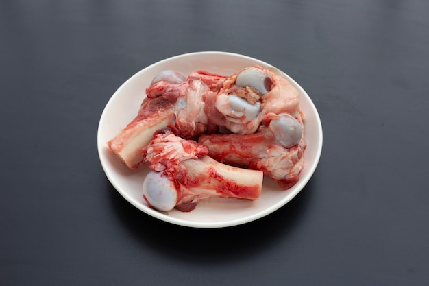 Raw pork bones in white plate on dark background.