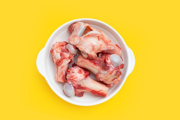 Raw pork bones in white plate on yellow background.